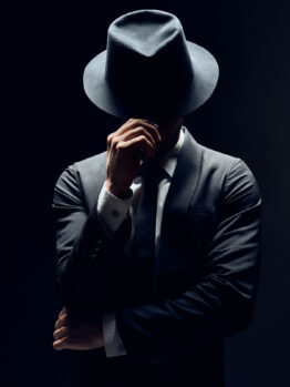 Man in suit hiding face behind his hat isolated on dark background